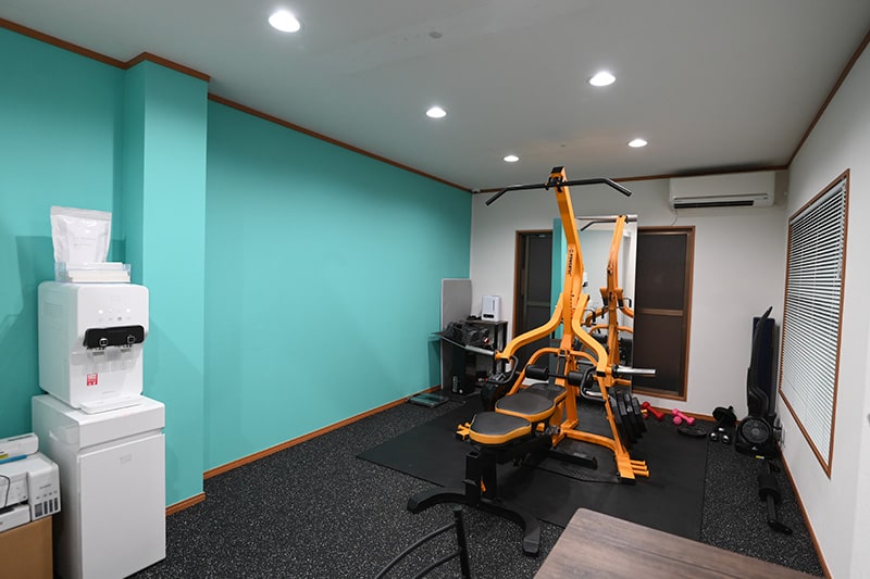 Apple GYM（アップルジム）北千住店の青い壁が特徴の店内とトレーニング機材、カウンセリングスペース、ウォーターサーバーの写真
